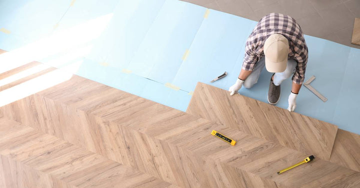 A contractor installs wide planks of laminate flooring that features a chevron pattern on the floor of a home.