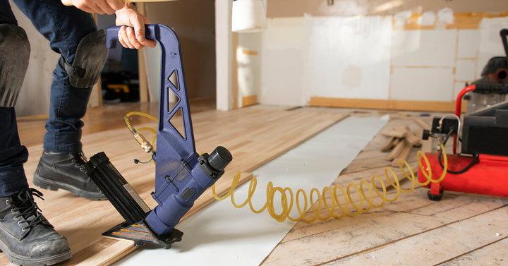 A professional hardwood flooring installer uses a nail gun to install the wood planks on the floor of a room.