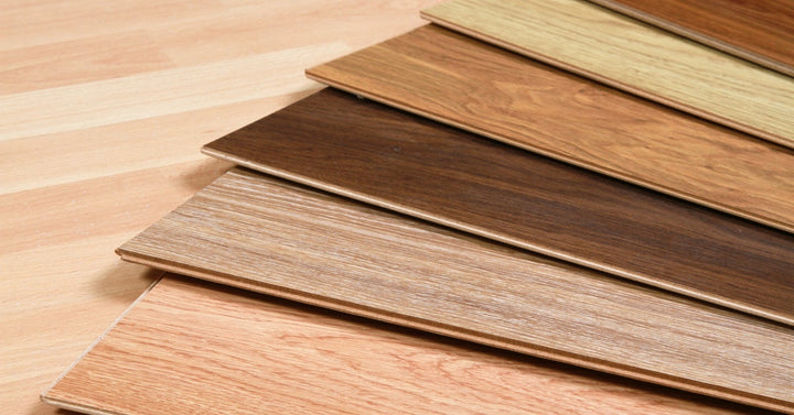 Seven wooden floor samples fan out across a light laminate surface. The planks vary in color from pale to dark tones.